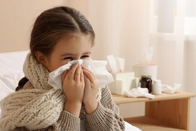 Little girl sitting in bed feeling sick with signs of a cold.
