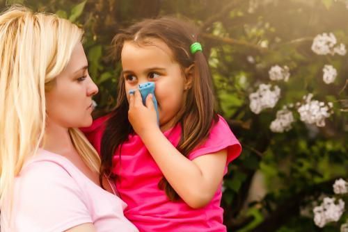 A child sneezing from spring allergies while looking at her mother.