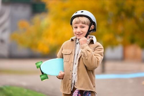 Child holding a skateboard while wearing protective helmet for safety