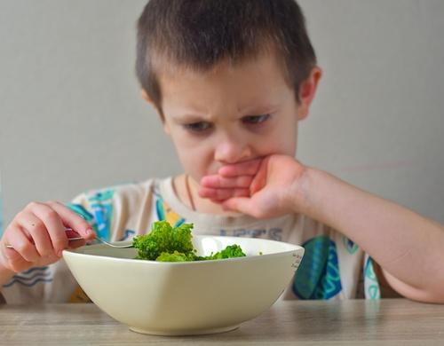 Picky eater child looking dissatisfied while viewing broccoli, illustrating food aversion, selective eating habits, and challenges with encouraging healthy nutrition.